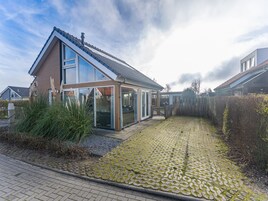 Una casa moderna con techo inclinado, ventanas amplias y un camino de entrada pavimentado.