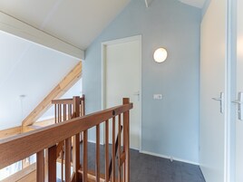 Uma escadaria com corrimãos de madeira que leva a um quarto com parede azul clara e uma porta branca.