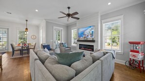 A living room with a grey sofa, a TV mounted on the wall, a ceiling fan, and a fireplace. - YOUR BEST BEACH VACATION EVER  POOL GOLF CART BIKES VERY CLOSE TO BEACH (Santa Rosa Beach)