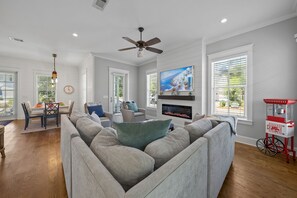 A living room with a grey sofa, a TV mounted on the wall, a ceiling fan, and a fireplace. - YOUR BEST BEACH VACATION EVER  POOL GOLF CART BIKES VERY CLOSE TO BEACH (Santa Rosa Beach)