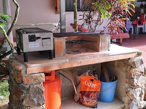 An outdoor cooking area with a brick oven, a gas cylinder, and a bag of charcoal. - Bungalow with a large pool, nestled in a garden with lush, exotic vegetation (Las Terrenas)