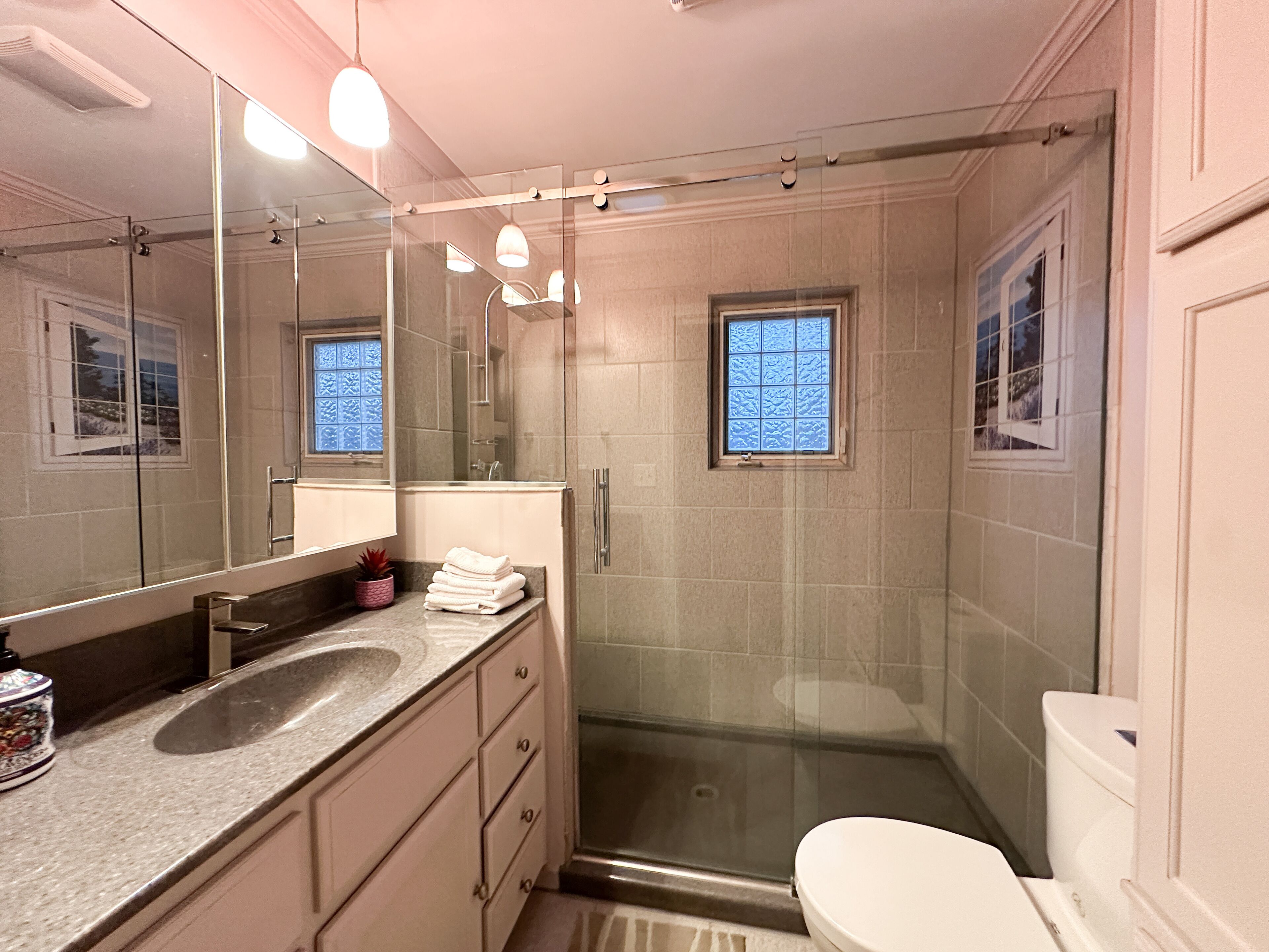 A modern bathroom with a glass-enclosed shower, a large mirror, and a window.