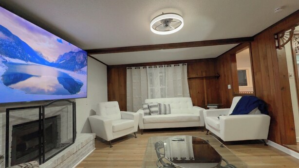 A living room with a fireplace, white sofas, a glass coffee table, and a large TV screen displaying a mountain scene. - Resort-Style Retreat w/ Pool, Prime OP Location (Mission)