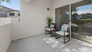 A balcony with two chairs, a potted plant, and a glass door leading to a patio area. - Scottsdale Desert Escape 2BR with Sunrise Peak Views, Pets OK (Scottsdale)