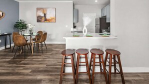A modern kitchen with a white island, bar stools, and a dining area with a table and chairs. - Scottsdale Desert Escape 2BR with Sunrise Peak Views, Pets OK (Scottsdale)