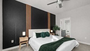 A modern bedroom with a large bed, a nightstand, a ceiling fan, and a view into the bathroom. - Scottsdale Desert Escape 2BR with Sunrise Peak Views, Pets OK (Scottsdale)