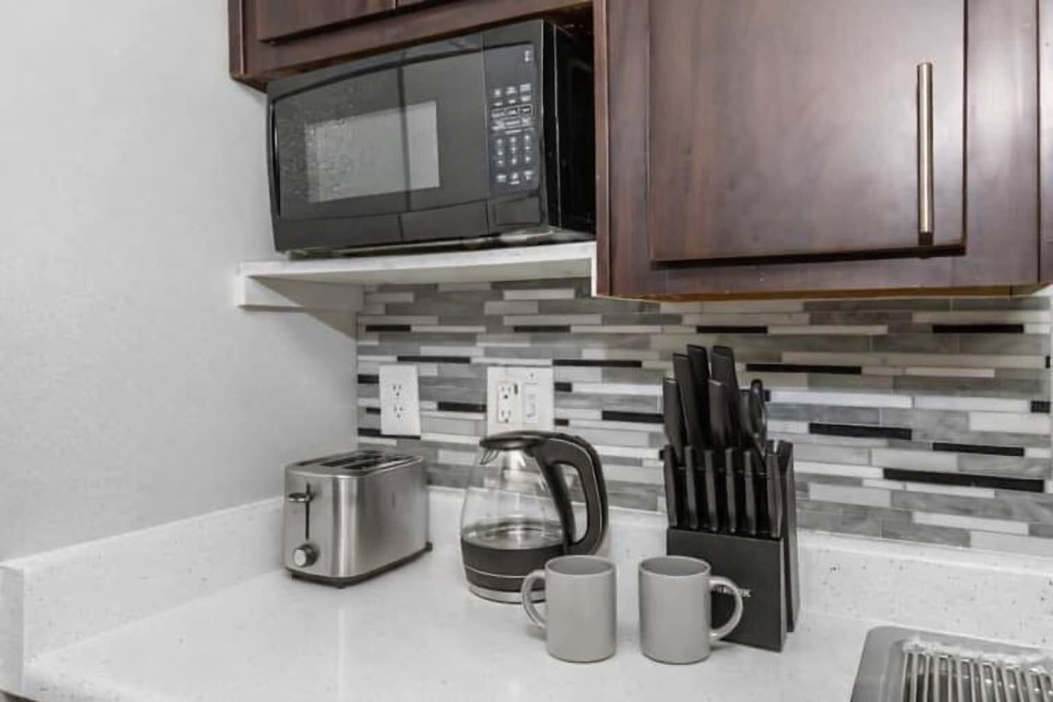 A kitchenette with a microwave, toaster, coffee maker, and mugs on the counter.