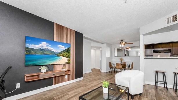 Un salon moderne doté d’un téléviseur à écran plat, d’un mur recouvert de panneaux en bois, d’un coin repas, d’une cuisine et d’un ventilateur de plafond.