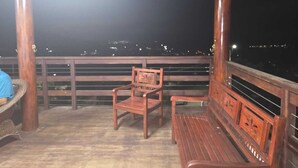 Una terraza de madera con un banco y una silla, con vista a un paisaje urbano nocturno.