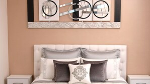Un dormitorio con cabecera capitonada, cama con varios almohadones y una obra de arte colgada sobre la cama.