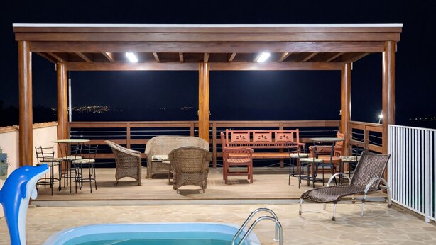 Un área de piscina al aire libre con una pérgola de madera, muebles de mimbre y vistas de la ciudad de noche.