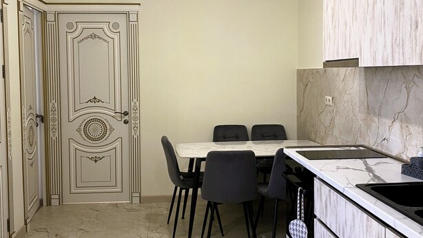 A compact kitchen with a dining table, chairs, a countertop with a sink, and a decorative light fixture.