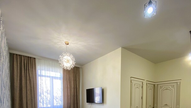 A living room with a sofa, a TV, a ceiling light, and a door.