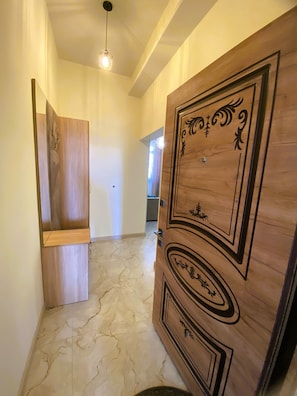 Un pasillo con puerta de madera que presenta intrincados grabados, una lámpara y suelo de mármol.
