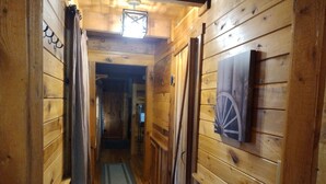 A wooden hallway with a checkered curtain, a rug, and a wall-mounted picture of a wagon wheel. - Back Country Roads Rustic Escape (Jumping Branch)