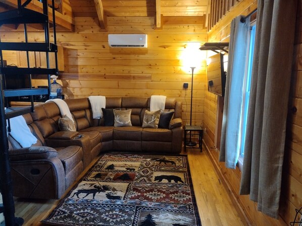 A cozy log cabin interior with a sectional sofa, a patterned rug, and a wooden ceiling.