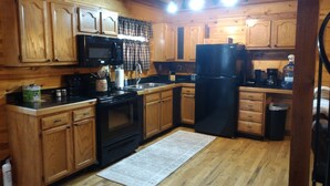 A kitchen with wooden cabinets, a black refrigerator, a stove, and a microwave. - Back Country Roads Rustic Escape (Jumping Branch)