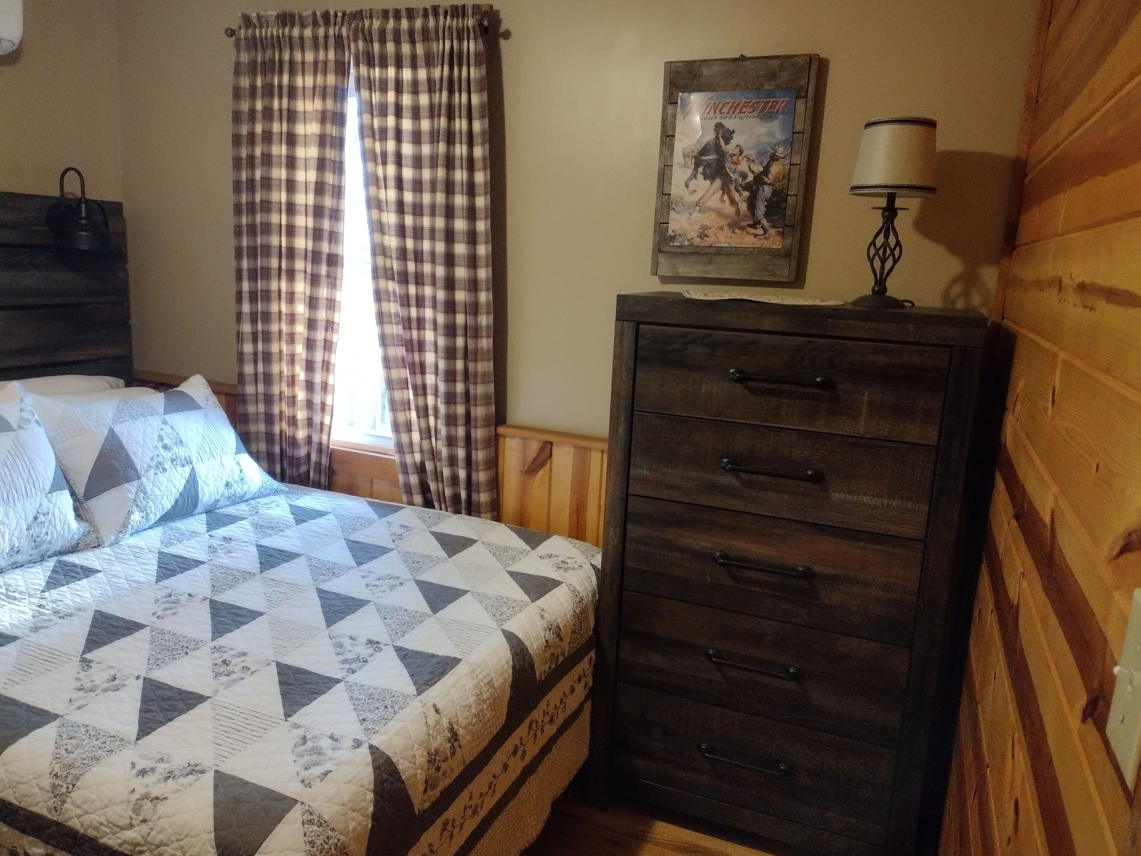 A bedroom with a bed, a dresser, a lamp, and a poster on the wall.