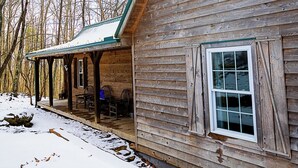 A wooden cabin with a porch and a window, surrounded by snow and trees. - Back Country Roads Rustic Escape (Jumping Branch)