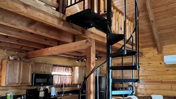 A wooden interior with a spiral staircase, a kitchen area, and a seating area with a sofa. - Back Country Roads Rustic Escape (Jumping Branch)