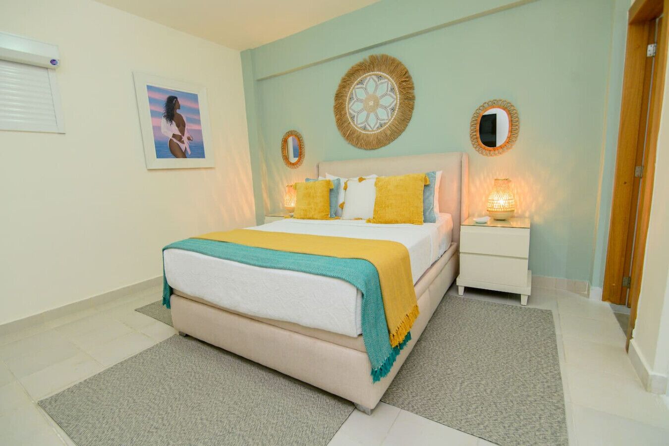 A bedroom with a bed, bedside tables, a wall-mounted mirror, and a framed picture.