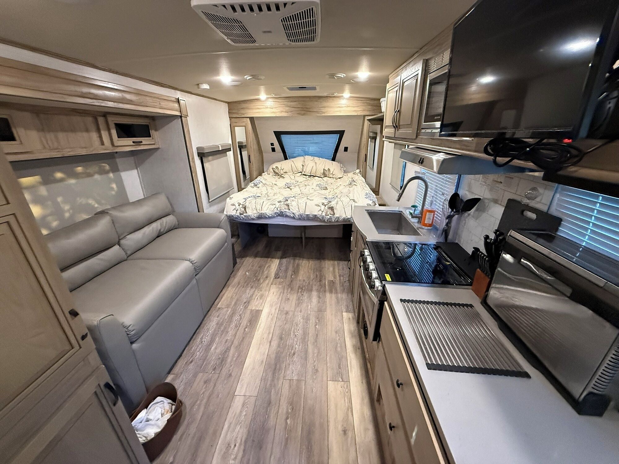 Interior compacto de una caravana con kitchenette, cama con colcha estampada, zona de estar y televisor.