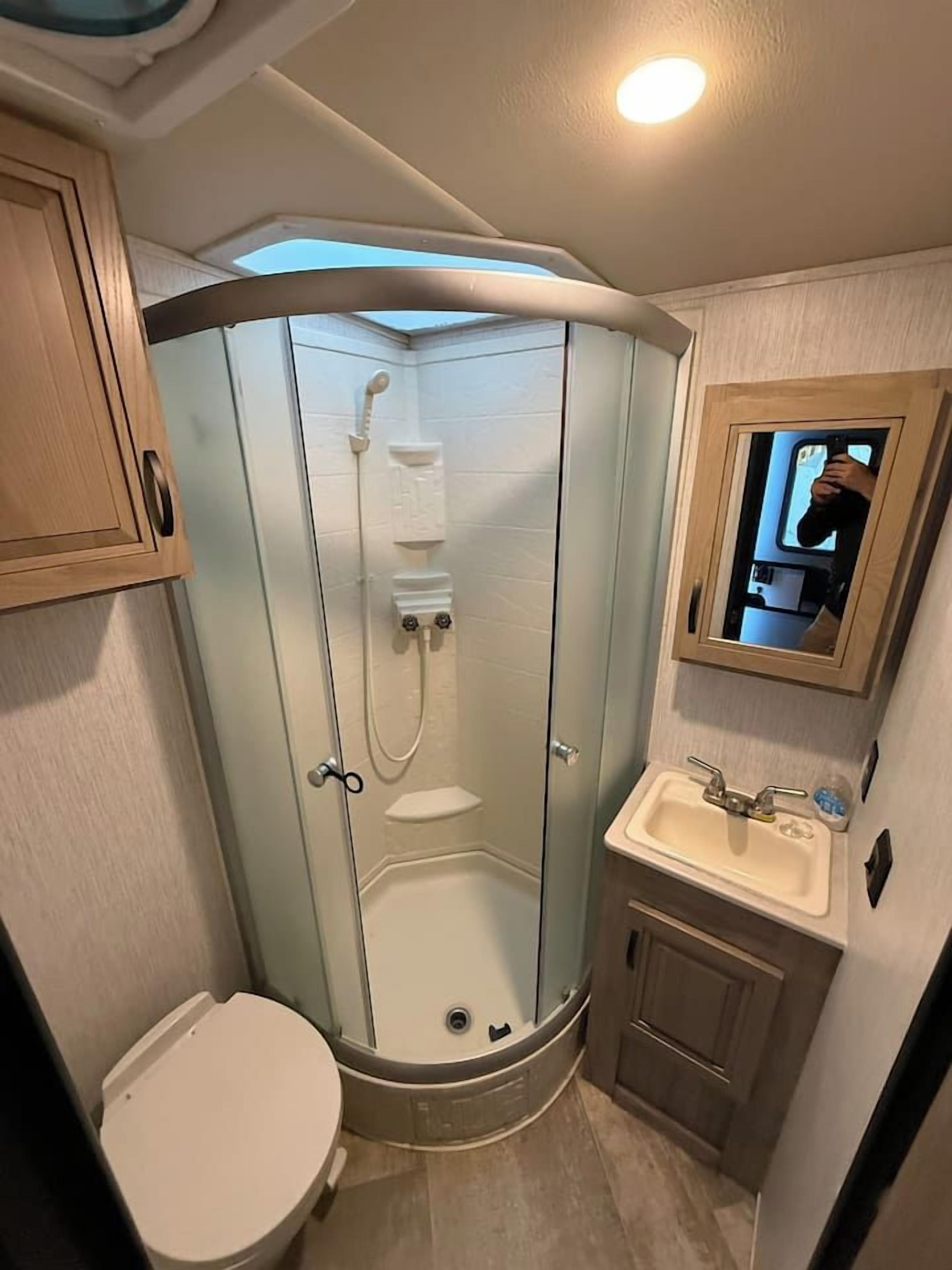 Un baño pequeño con ducha compartimentada por vidrio, inodoro y lavamanos.