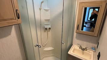 Un baño pequeño con ducha compartimentada por vidrio, inodoro y lavamanos.