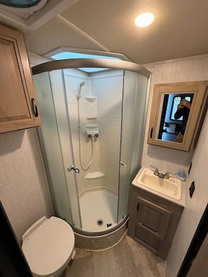Un baño pequeño con ducha compartimentada por vidrio, inodoro y lavamanos.