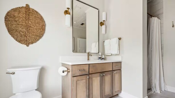 Un bagno con il water, un lavandino con specchio, mobiletti in legno e una tenda da doccia.