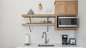 Una cucina moderna con forno a microonde integrato, macchina del caffè e tostapane. Si nota un lavello con rubinetto e pensili in legno sopra il piano di lavoro.