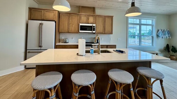 A modern kitchen with wooden cabinets, a large island with bar stools, a refrigerator, and a window with a view. - #3 Yellow Lakeview Suite A (Garrison)