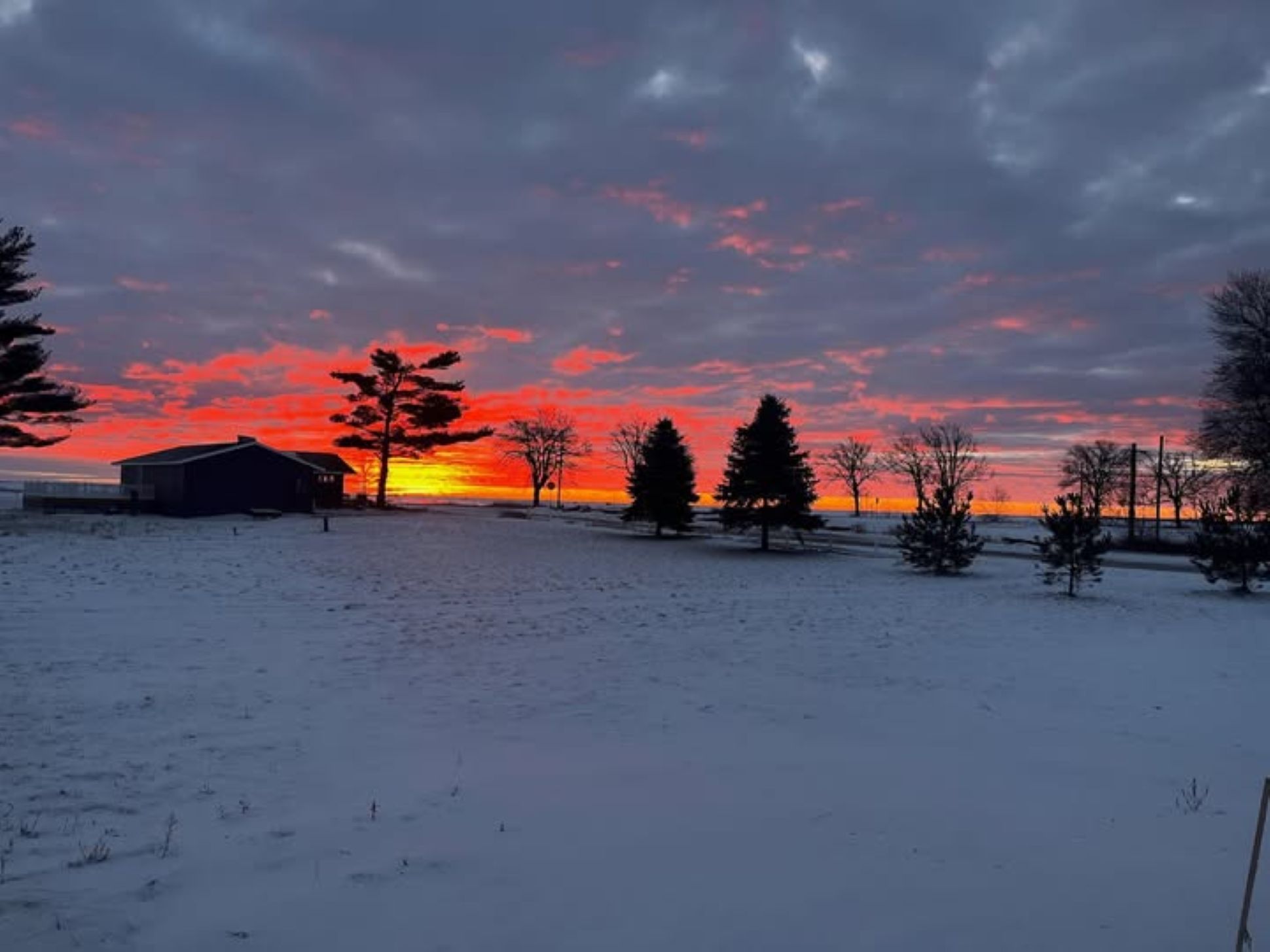 A snowy landscape with a sunset, trees, and a building.