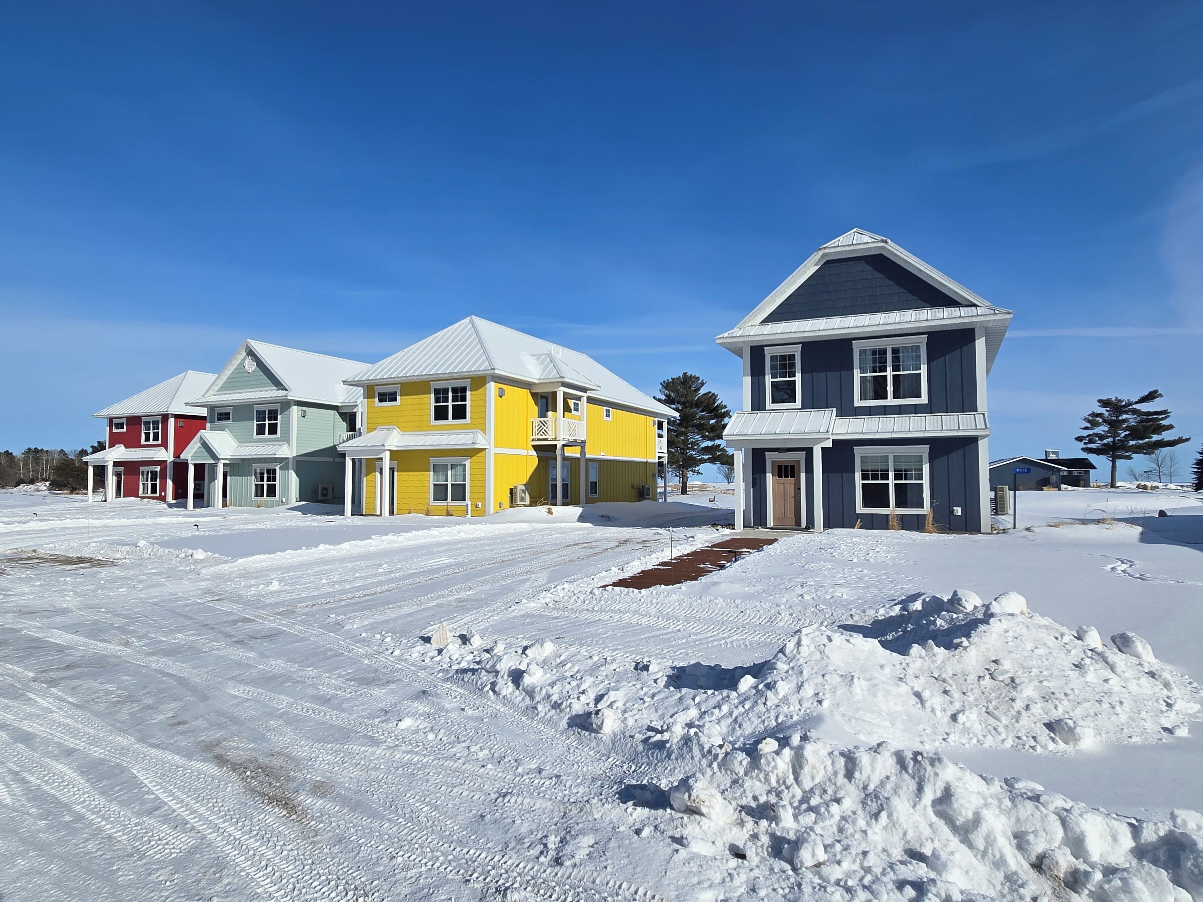 A residential area with houses in various colors, a clear sky, and snow-covered ground.
