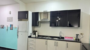 Eine moderne Küche mit einem weißen Kühlschrank, schwarzen Schränken, einem Gasherd und einer Spüle aus Edelstahl.