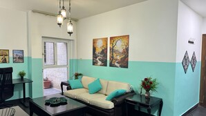 Ein Wohnzimmer mit einer Couch, Couchtisch und Dekoration. An den Wänden befinden sich Gemälde und ein Fenster mit Blick.
