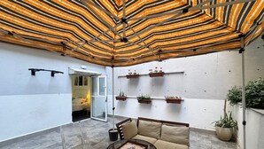 Ein moderner Patio-Bereich mit einer Streifenmarkise, einem Glastisch, einer gepolsterten Bank und Topfpflanzen.