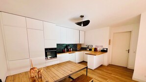 Uma cozinha moderna com armários brancos, uma mesa de jantar de madeira e forno embutido.