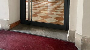 En hotellentrén med ett rutmönstrat golv, en röd matta och en glasdörr som leder till en hiss.