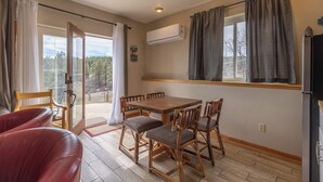 En matplats med ett träbord och stolar, en röd läderfåtölj, en skjutdörr i glas som leder ut till en balkong och en luftkonditioneringsenhet på väggen.