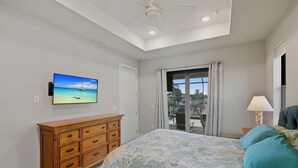 A bedroom with a bed, a dresser, a TV, a balcony with a view, and a ceiling fan. - Sunset Retreat Pool/Spa, great views, we love dogs (Punta Gorda)