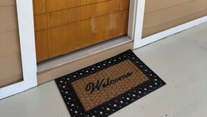 Una puerta de madera con un panel de vidrio, un felpudo con la palabra 'Welcome' y un buzón en la pared.