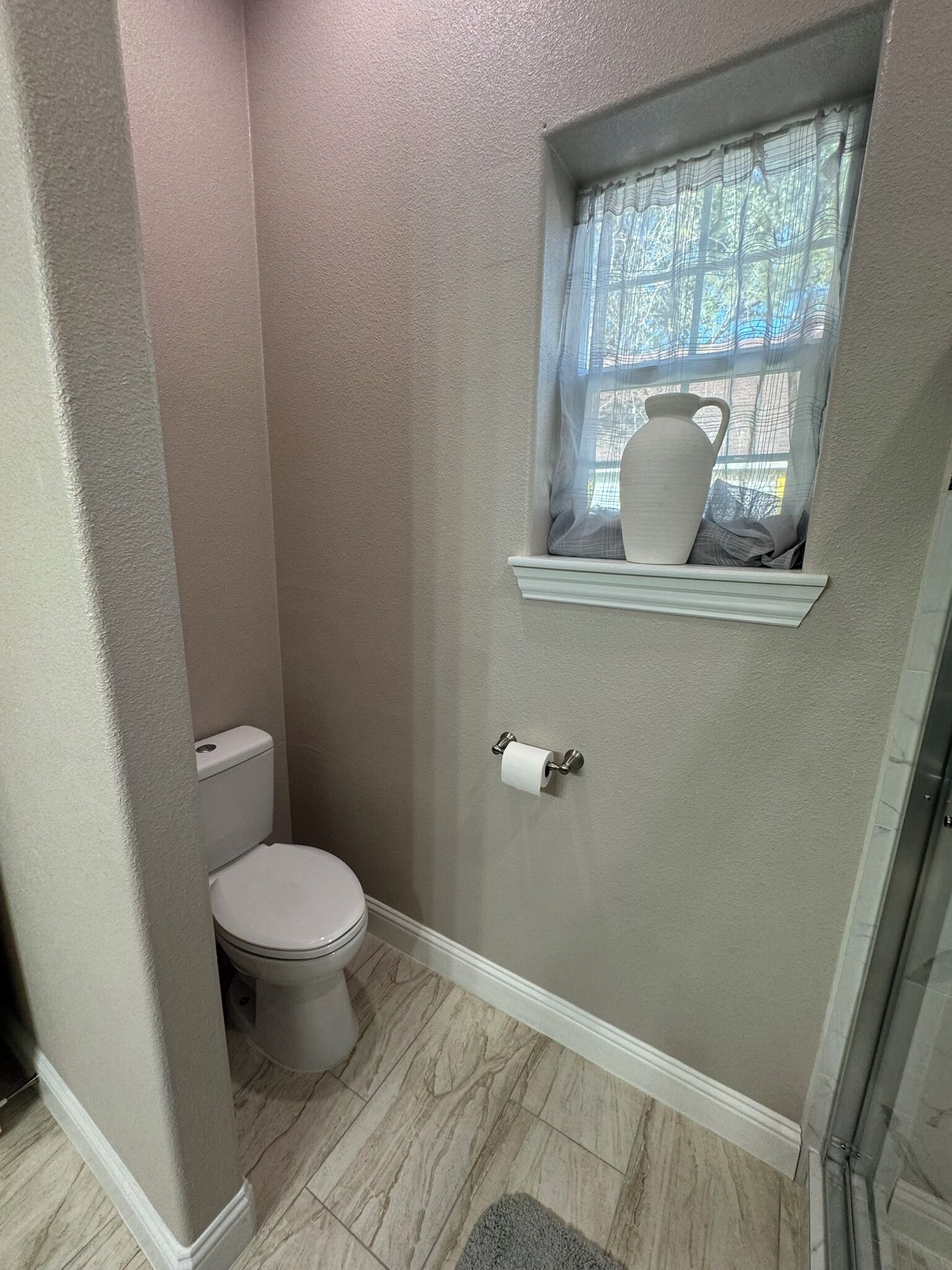 Een badkamer met toilet, douche en raam met gordijn.
