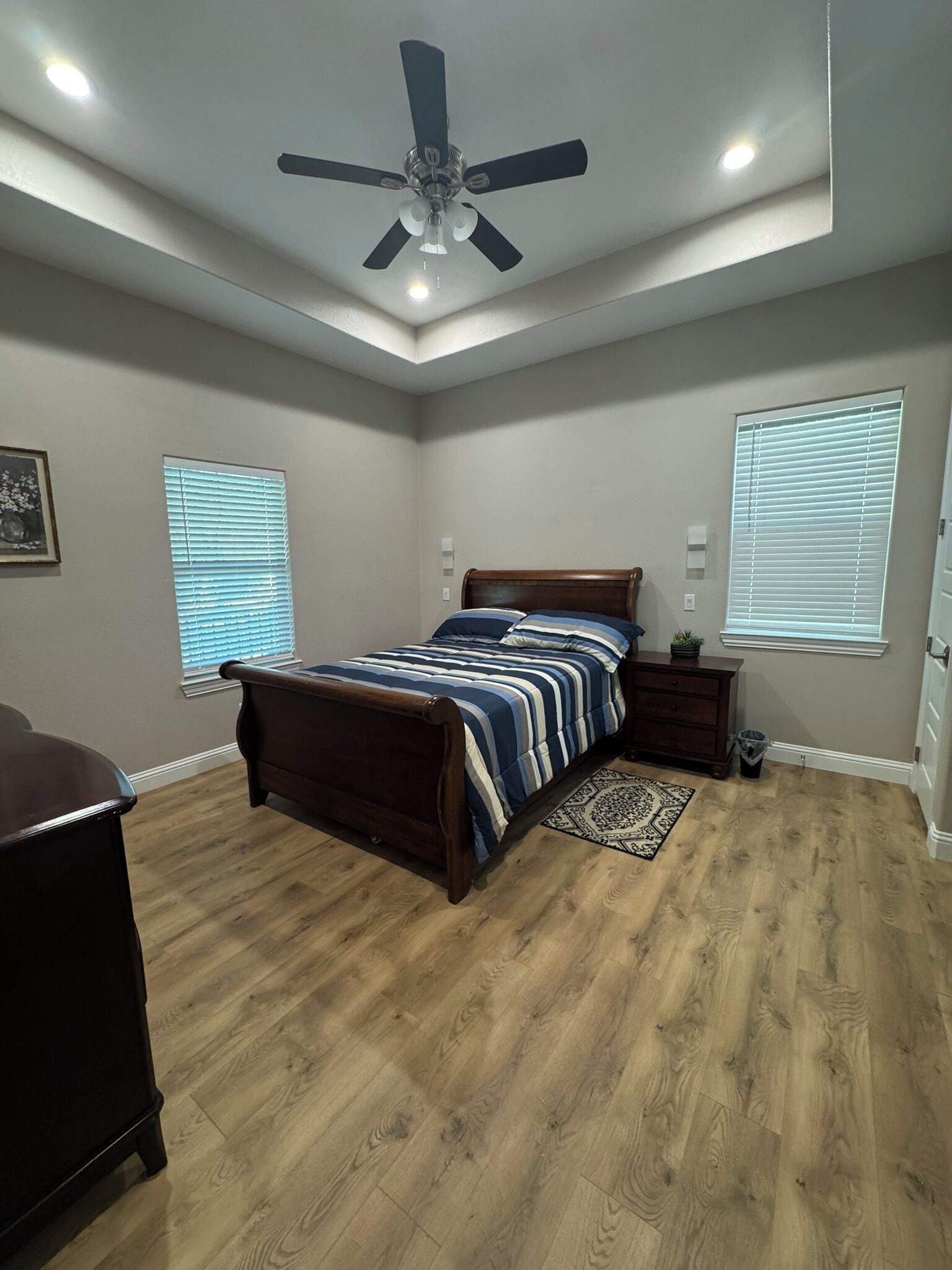 A bedroom with a bed, a ceiling fan, and two windows with blinds.