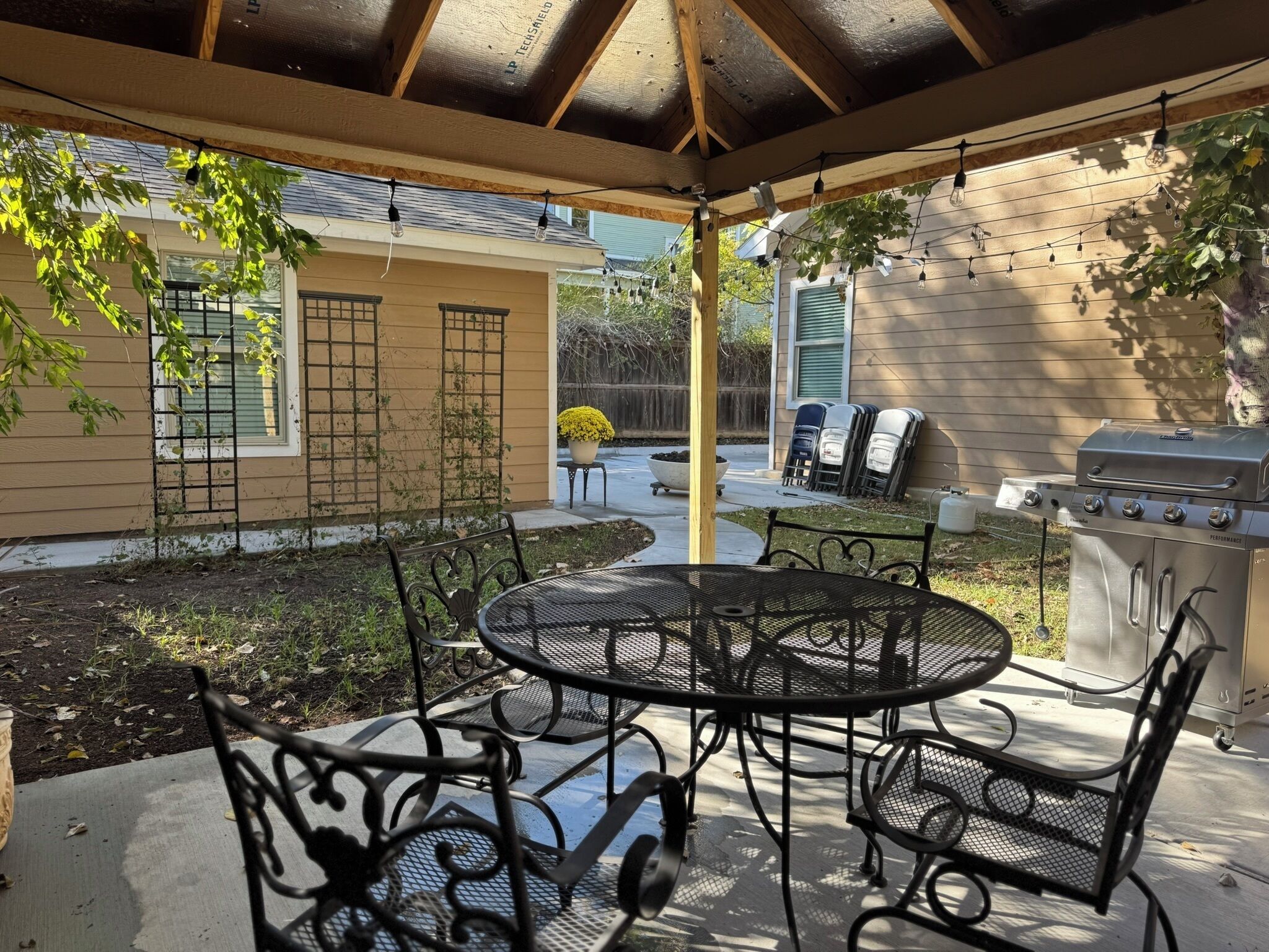 A covered patio with a round metal table and chairs, a barbecue grill, and a pergola with string lights.