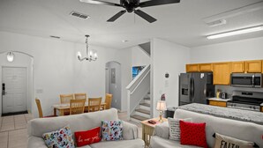 Ein modernes Wohnzimmer mit einer Sofagarnitur, einem Essbereich mit Stühlen, einer Küche mit Holzschränken und einer Treppe.