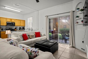 A living room with a sofa, ottoman, and a kitchen area with wooden cabinets and a microwave. - Family 3BR/3BA Home in Regal Palms Resort (Davenport)