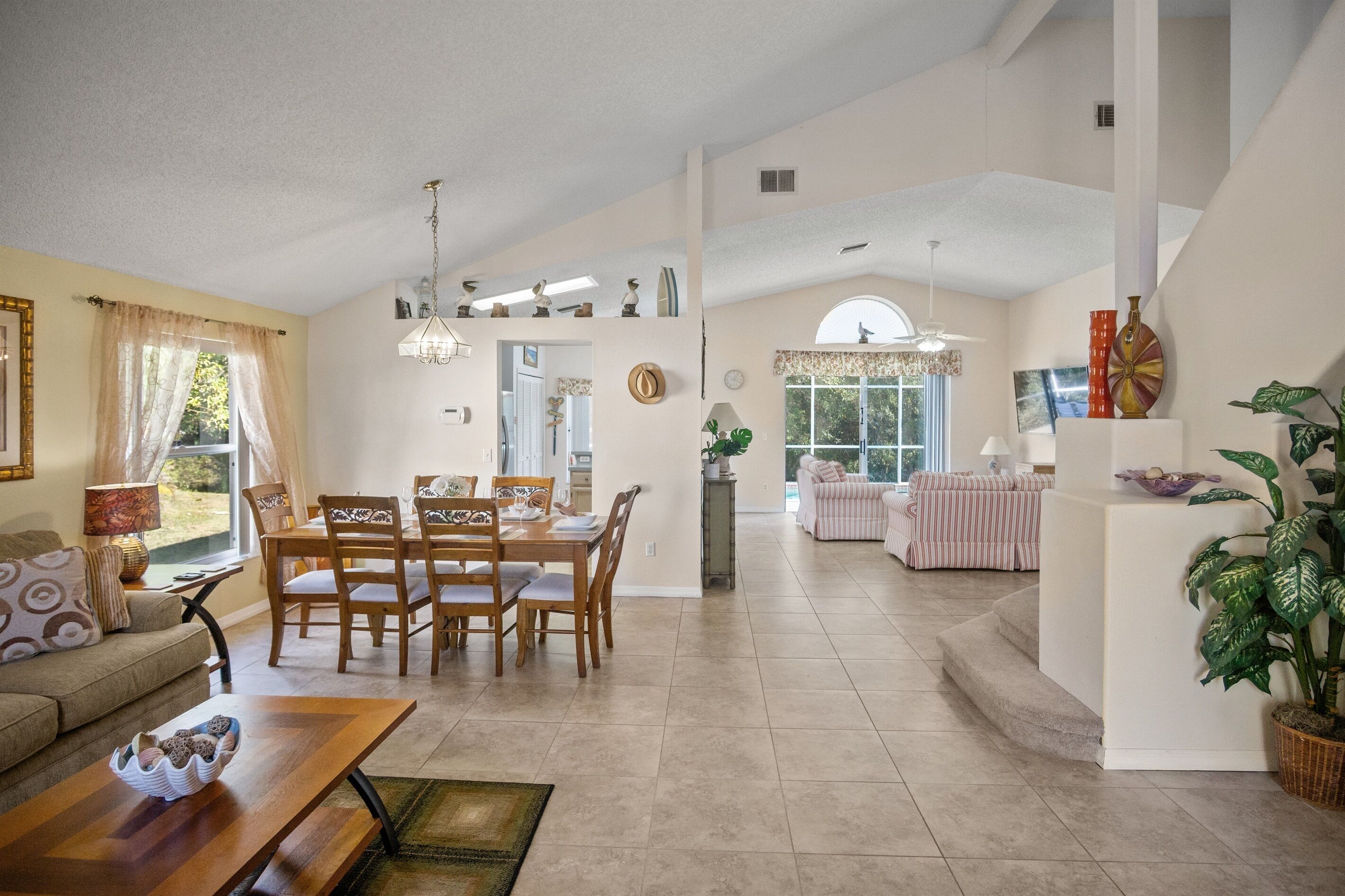 A spacious living area with a dining table and chairs, a sofa, and a large window.