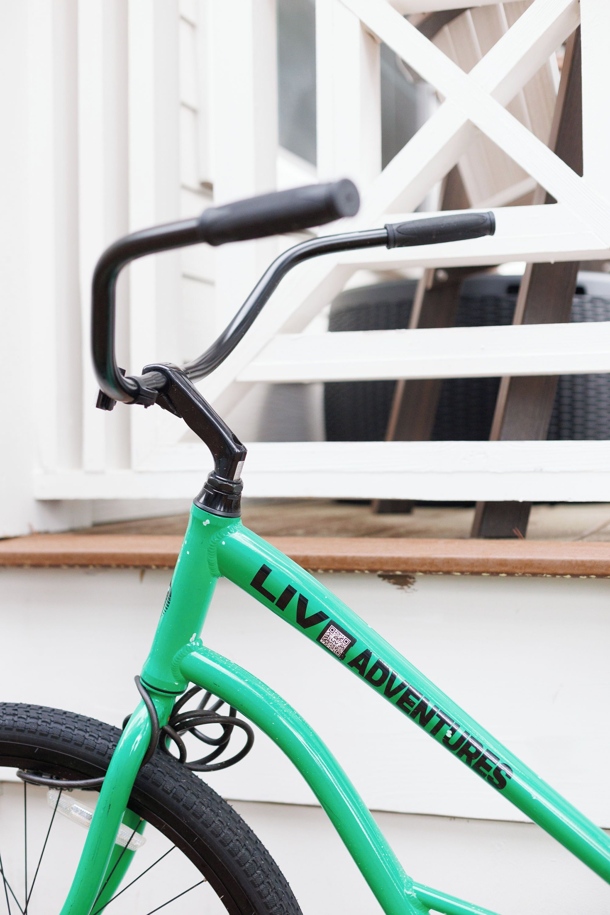 Una bicicleta verde con la leyenda 'LIV ADVENTURES' en el cuadro, ubicada frente a un ventanal blanco con diseño de celosía.