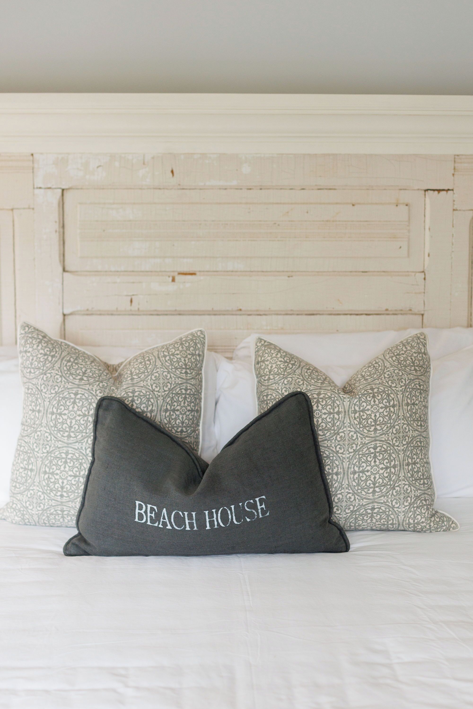 Una cama con almohadas estampadas y una almohada con el texto 'BEACH HOUSE'.